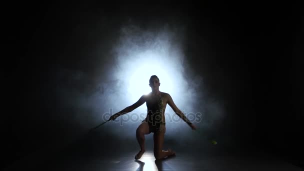 Rhythmische Sportgymnastin wirft Keule hoch und fängt sie ein. schwarzer Hintergrund. Licht hinten. Silhouette - Filmmaterial, Video