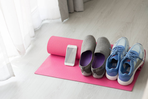 Blue, gray and purple Sport shoes, yoga mat, smartphone on gray  - Фото, изображение