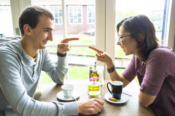 Jeune homme et femme se pointant du doigt alors qu'ils étaient assis au café
 - Photo, image