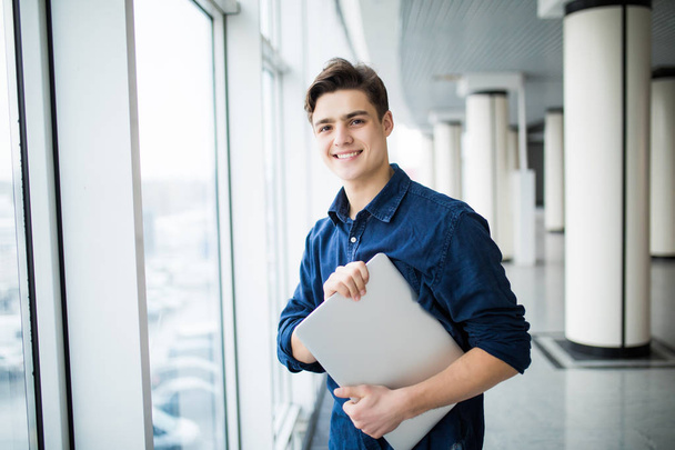 Handsome man holding a laptop in hall - Photo, Image