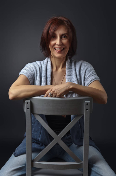 portrait of middle aged woman on a gray chair - Photo, Image