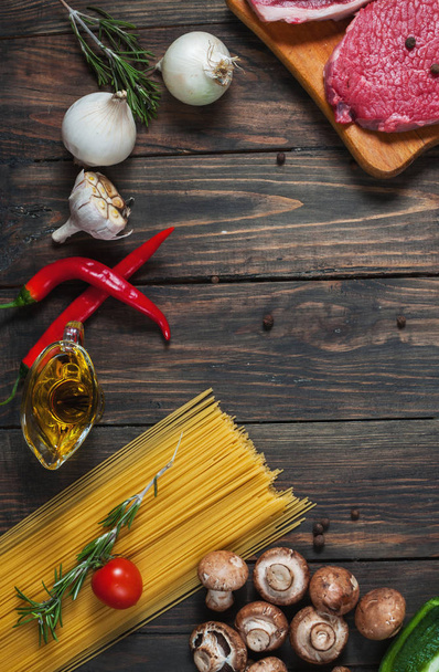 Rauwe biefstuk met pasta, tomaten, champignons en kaas op donkere tafel achtergrond, bovenaanzicht. copyspace - Foto, afbeelding