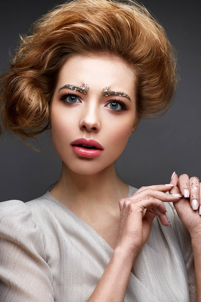 Young girl with lush hairstyle and make-up Nude. Beautiful model with sequins on the eyebrows and delicate pink manicure.  - Фото, изображение