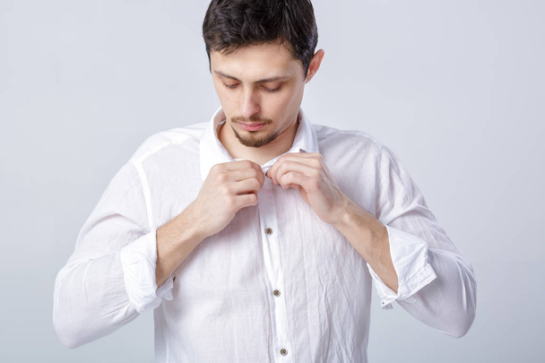 portrait of young brunette man in white shirt buttoning on grey - Photo, Image