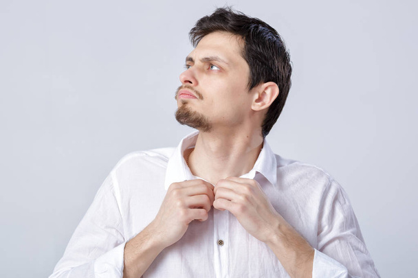 portrait of young brunette man in white shirt buttoning on grey - Fotó, kép