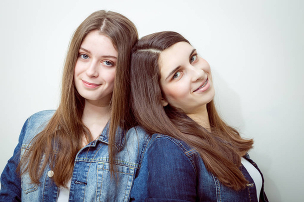 Closeup portrait of two beautiful young women with long dark hair and natural makeup wearing jeans shirts happy smiling looking at camera - Zdjęcie, obraz
