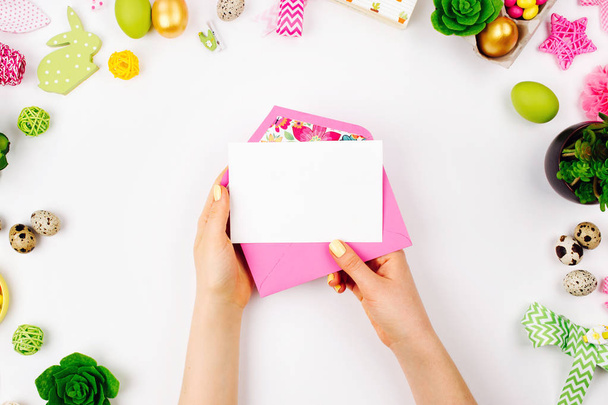 Woman holding a empty card and pink envelope. Beautiful spring mock up.  Easter concept.  Flat lay, top view - Foto, Imagen