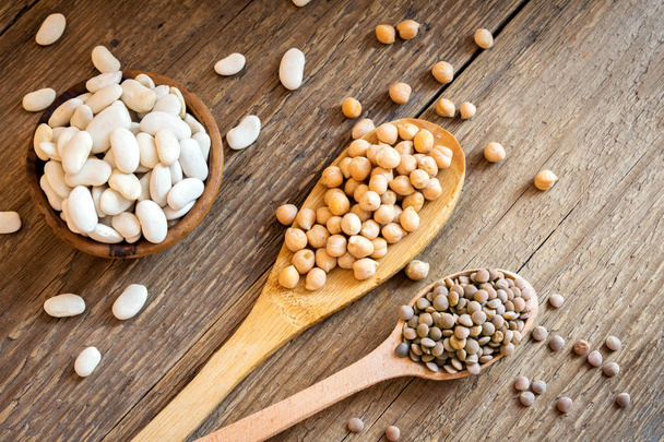 Assorted Legumes (chickpeas, green lentils, white beans) over rustic wooden background - ingredient for healthy vegan, vegetarian, diet food meal, vegetable protein - Photo, Image