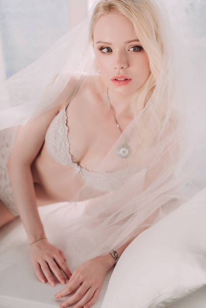 Beautiful sexy lady in elegant white lingerie wearing wedding veil. Portrait of fashion model girl indoors. Beauty blonde woman in lace lingerie. Female body in underwear. Studio retouched shot - Fotografie, Obrázek