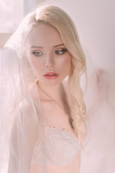 Beautiful sexy lady in elegant white lingerie wearing wedding veil. Portrait of fashion model girl indoors. Beauty blonde woman in lace lingerie. Female body in underwear. Studio retouched shot - Fotografie, Obrázek