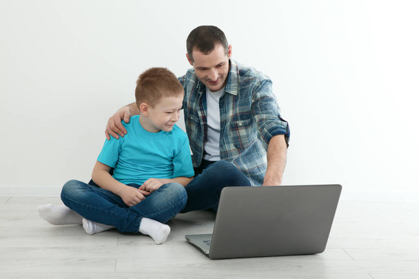 Father and son using laptop sitting on the hardwood floor togeth - Zdjęcie, obraz