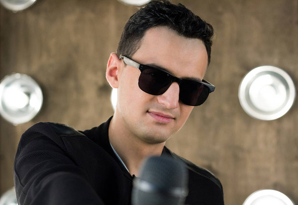 Чоловіча співачка в сонцезахисних окулярах з мікрофоном виступає в проекторах
 - Фото, зображення