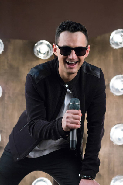 Güneş gözlüklü erkek şarkıcı mikrofon şarkı projektörler ile  - Fotoğraf, Görsel