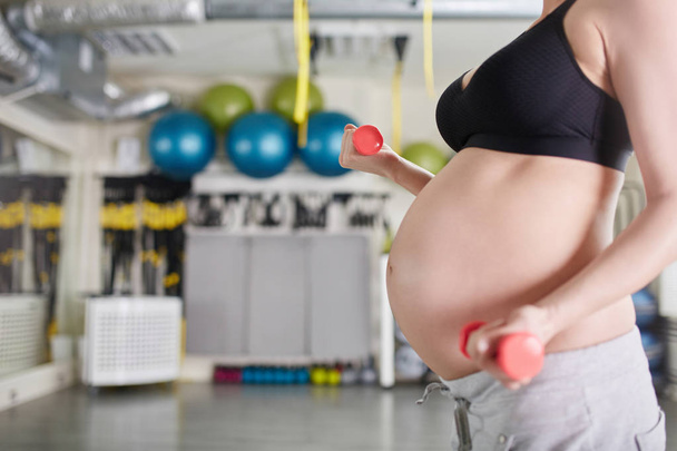 Pregnant woman lifting weights at gym - Фото, изображение