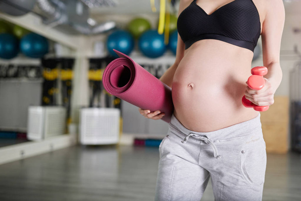 Pregnant woman at gym holding weights and mat - Photo, Image