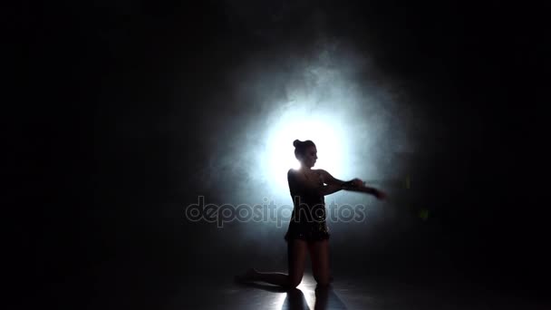 Ritmisch gymnaste werpt foelie en vangt haar. Zwarte achtergrond. De achterzijde van het licht. Silhouet. Slow motion - Video