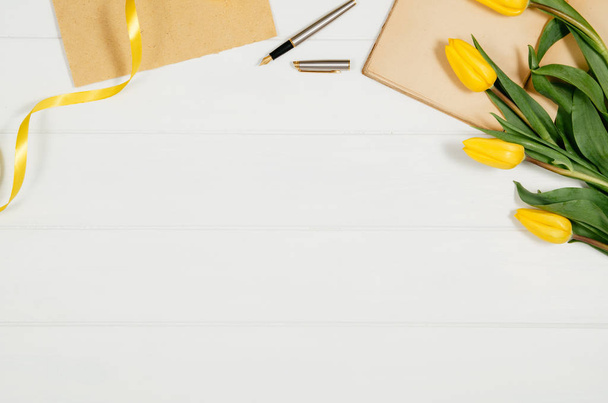 Hintergrund mit gelben Tulpen, leerer Notizblock auf weißem Holztisch - Foto, Bild