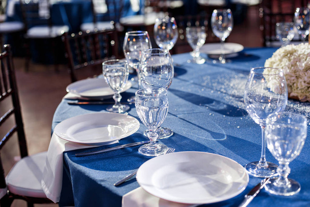 Mariage. Un banquet. Les chaises et la table ronde pour les invités, servis avec couverts et vaisselle et recouverts d'une nappe bleue
. - Photo, image
