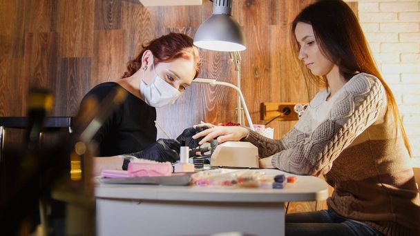 Mestre de unhas em máscara médica fazendo manicure profissional para o modelo branco caucasiano, salão de beleza
 - Foto, Imagem