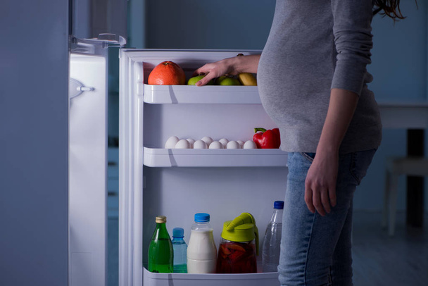 Pregnant woman near fridge looking for food and snacks at night - Фото, изображение