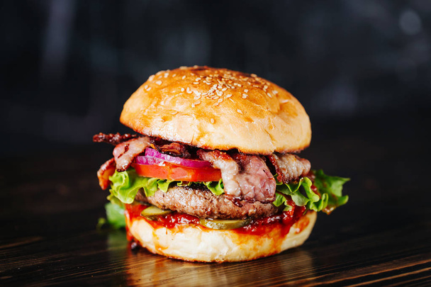 Burger with bacon, meat, tomato and lettuce   on wooden background. Close up - Foto, immagini
