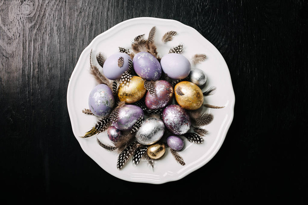 Beautiful Easter eggs and feathers with a dish on a black wooden background - Foto, imagen