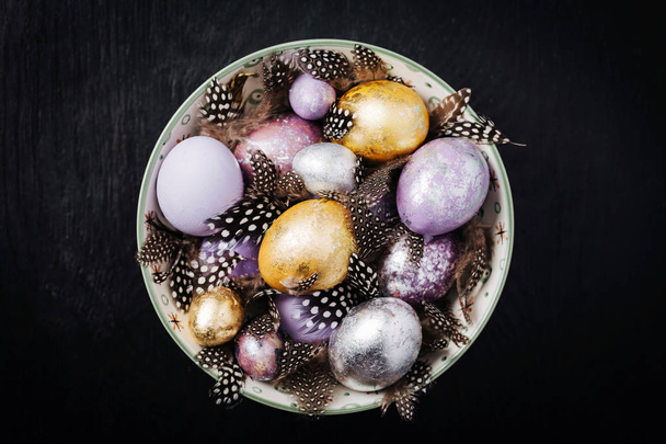 Beautiful Easter eggs and feathers with a dish on a black wooden background - Foto, Bild