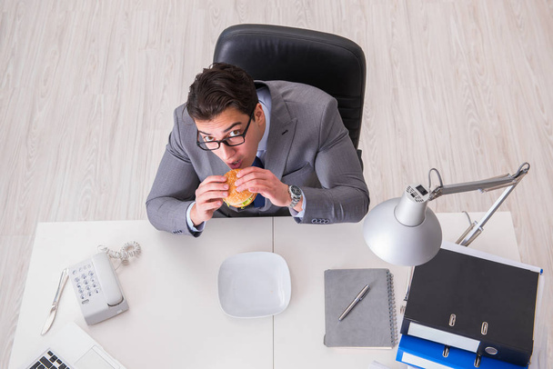 空腹面白いビジネスマンがジャンクフードサンドイッチを食べる - 写真・画像