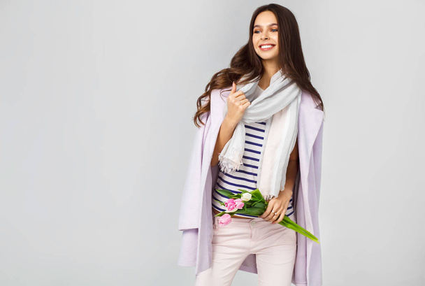 Fashion photo of a beautiful young woman with tulips in her hand .she dressed  in a beautiful coat, scarf, pants and T-shirt with stripes - Foto, Bild
