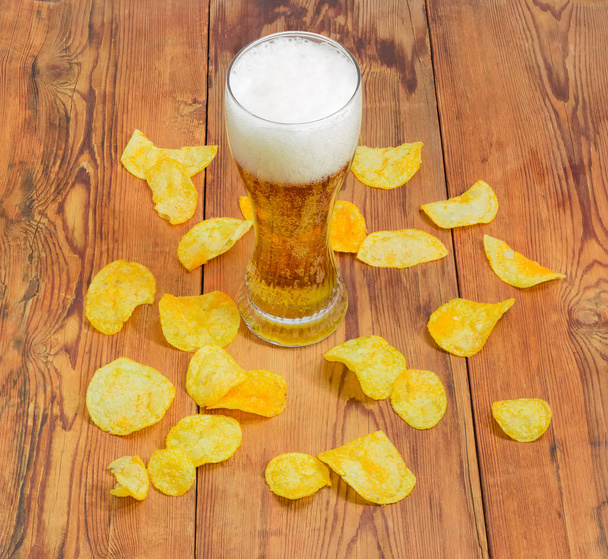 Lager beer among potato chips scattered on the wooden surface - Photo, Image