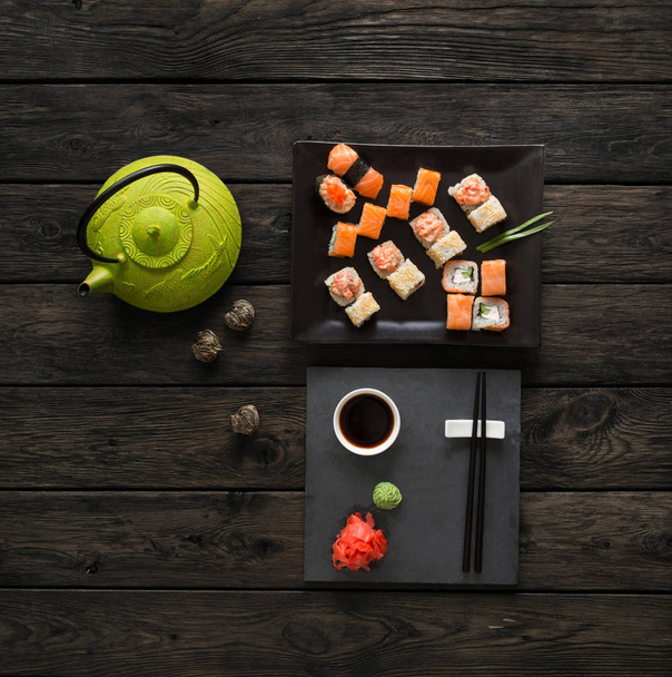 Conjunto de sushi e rolos com bule em madeira rústica preta, vista superior
 - Foto, Imagem