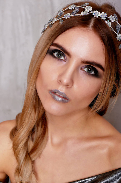 Beautiful girl model in the Studio shooting beauty. Silver makeup, hair in a sloppy spit, silver top. Cold - Photo, Image