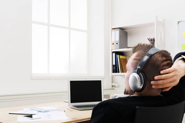 Over shoulder shot of businessman in office listen music in headphones - Foto, afbeelding