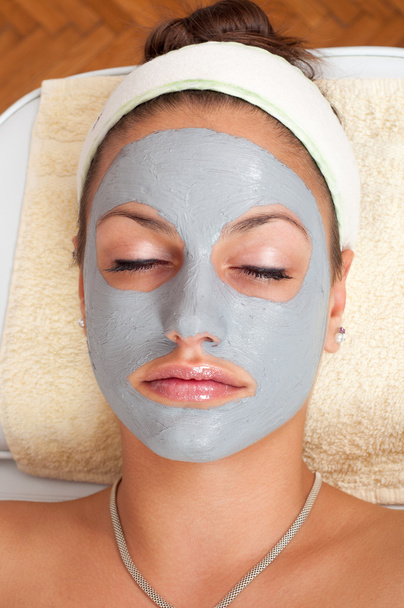 mooie jonge vrouw liggend op een massagetafel met natuurlijke gezichts masker op haar gezicht - Foto, afbeelding