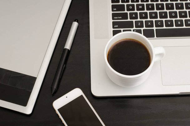 Filiżanka kawy, tabletu z rysikiem, część laptopa i telefon na czarny drewniany stół, zbliżenie - Zdjęcie, obraz