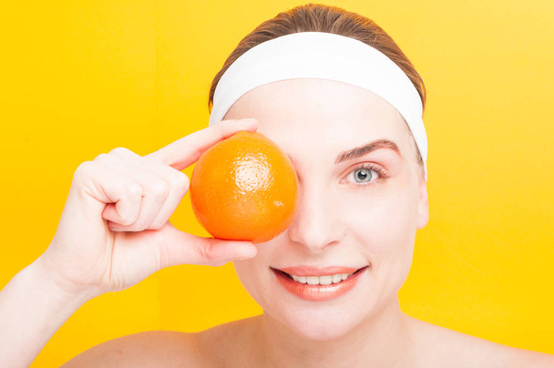 Mujer joven sosteniendo una naranja sobre su ojo
 - Foto, imagen
