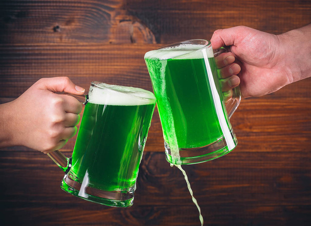 Mugs in hands with green beer  - Фото, изображение