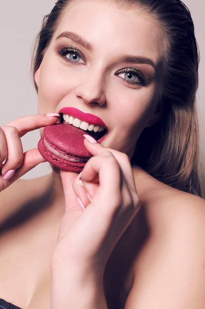 beautiful young woman with dark hair eating sweet macaroon  - Foto, Imagen