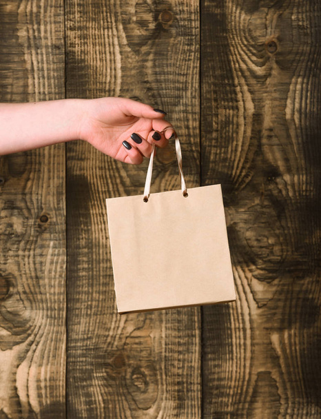 brown grey shopping bag in female hand on wooden background - Fotoğraf, Görsel