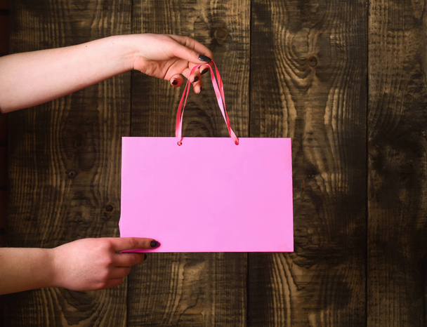 pink shopping bag in female hands on wooden background - Фото, зображення