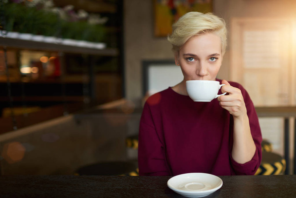 Hipster girl with trendy short haircut dressed in sweater drinking coffee for breakfast - Fotoğraf, Görsel