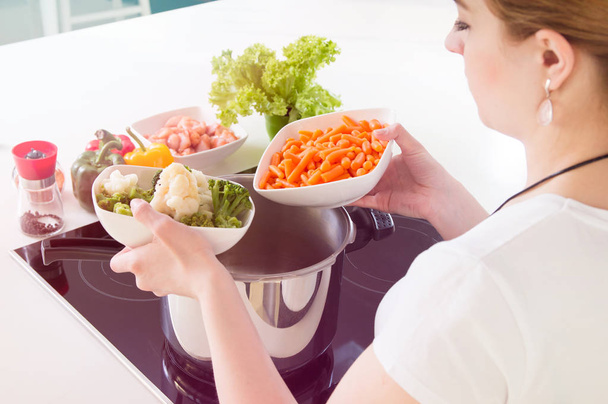 Woman puts vegetables into the pressure cooker. - Zdjęcie, obraz