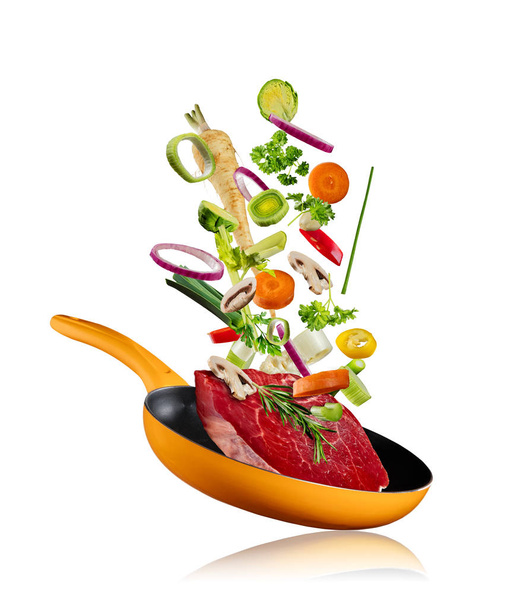 Fresh vegetables with steak flying into a pan on white background - Fotoğraf, Görsel
