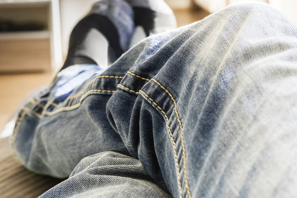Nahaufnahme von kreuzenden Beinen in Blue Jeans einer Person, die zu Hause auf dem Parkettboden liegt oder sitzt, Füße in Socken, aufgenommen vom Standpunkt des Fotografen - Foto, Bild