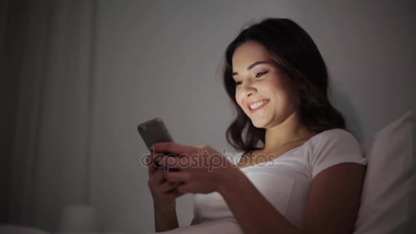 happy young woman with smartphone in bed at night - Кадры, видео