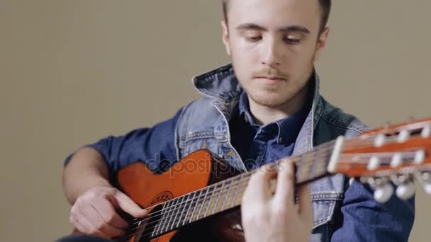 Guitarist playing on acoustic guitar sitting at gray wall background - Záběry, video