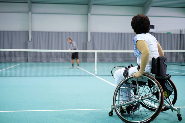 Vammainen kypsä nainen pyörätuolissa pelaa tennistä valmentajan kanssa
 - Valokuva, kuva