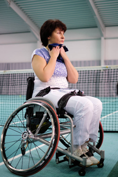 Κουρασμένος με αναπηρία ώριμη γυναίκα σε αναπηρικό καροτσάκι στο γήπεδο τένις. - Φωτογραφία, εικόνα