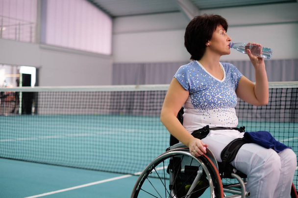 Sed discapacitada mujer madura en silla de ruedas en la cancha de tenis
. - Foto, Imagen