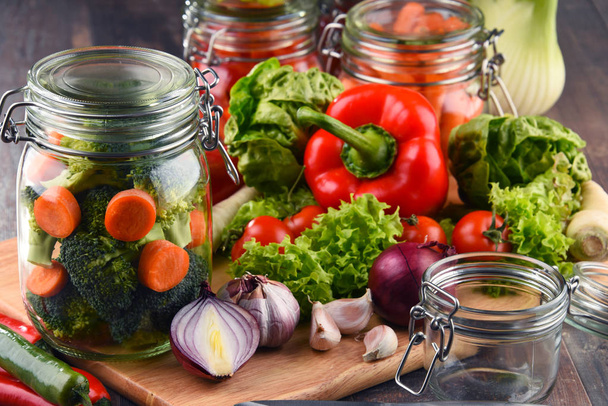 Üvegek, pácolt ételek és a nyers zöldségeket, vágódeszka - Fotó, kép